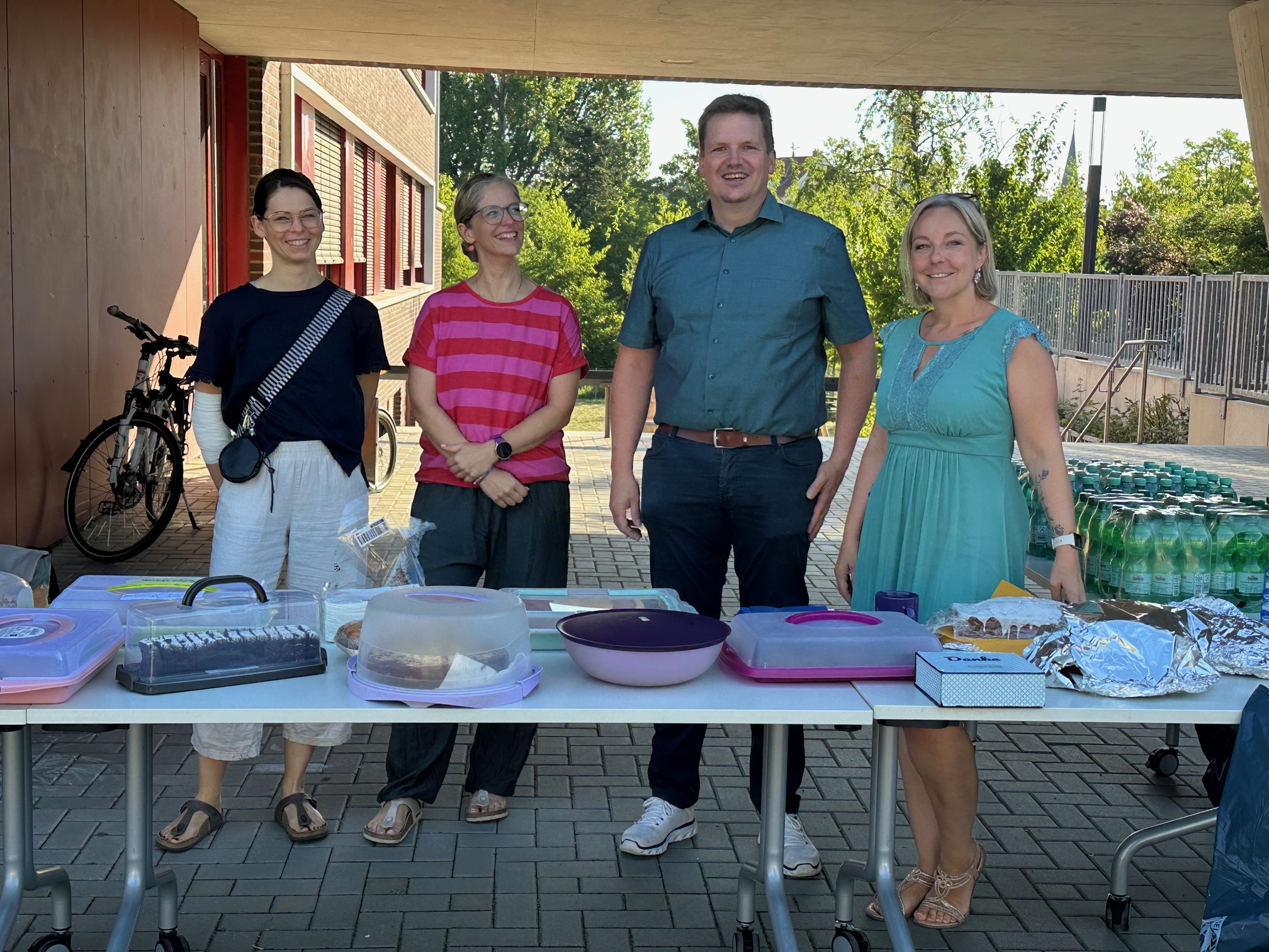 Zu sehen sind 4 Personen die hinter einer Kuchentheke stehen und freundlich in die Kamera lächeln